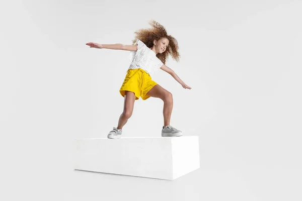 Retrato completo de menina sorridente em roupas casuais em pé na grande caixa isolada no fundo do estúdio branco. Conceito de infância feliz. — Fotografia de Stock