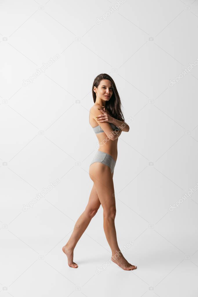 Portrait of young beautiful slim woman in grey lingerie,bra and panties posing isolated over gray studio background. Natural beauty concept.