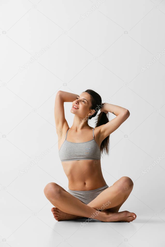Young adorable woman in lingerie sitting on floor isolated over gray studio background. Natural beauty concept.