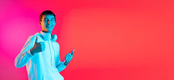 Leták s mladým mužem, studentem nebo chlapcem v neformálním oblečení s úsměvem izolovaný na pozadí studia magenta v neonu. Koncept lidských emocí. — Stock fotografie