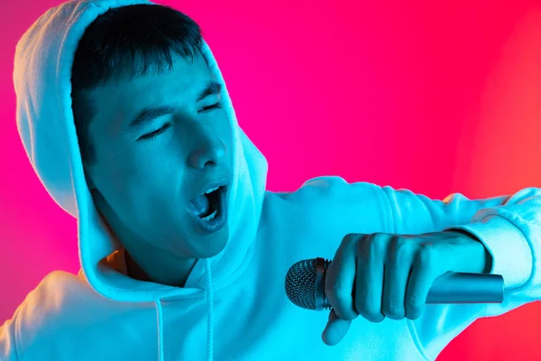 네온 에 있는 자홍색 스튜디오 뒤쪽에 고립된 마이크로폰 으로 노래를 부르고 있는 젊은 남자, 학생 혹은 소년의 모습. — 스톡 사진