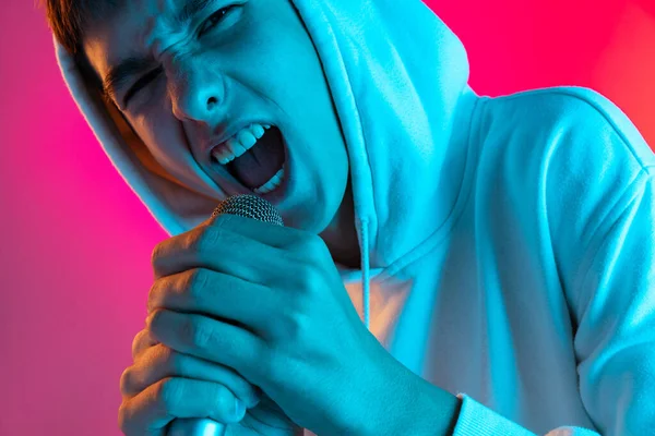 Porträtt av ung man, student eller pojke i avslappnade kläder sång med mikrofon isolerad på magenta studio backgroud i neon. — Stockfoto