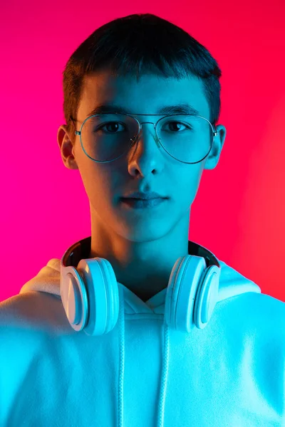 Πορτρέτο του νεαρού σοβαρού αγοριού, φοιτητής ή έφηβος κοιτάζοντας κάμερα απομονωμένη σε magenta studio backgroud σε neon. Αντίληψη ανθρώπινων συναισθημάτων. — Φωτογραφία Αρχείου