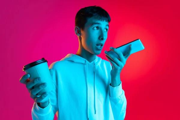 Studio ujęcie młodego chłopca, studenta, nastolatka w ubraniach casual za pomocą telefonu odizolowanego na tle magenta w neonowym świetle. — Zdjęcie stockowe