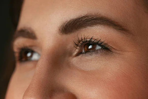 Крупным планом изображение женских карих глаз без макияжа изолировано на темном фоне студии. Концепция природной красоты. — стоковое фото