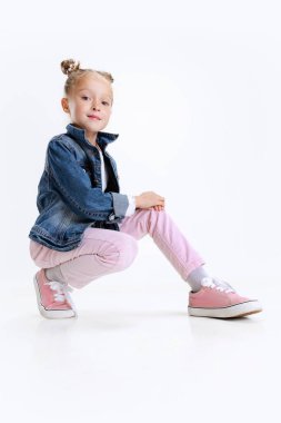 Beyaz stüdyo arka planında izole bir şekilde yerde oturan şık giyimli beyaz kız portresi..