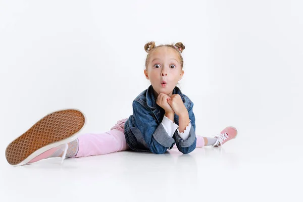 Портрет маленької кавказької милої дівчини в стильному одязі, що сидить на підлозі ізольованою на білій студії.. — стокове фото