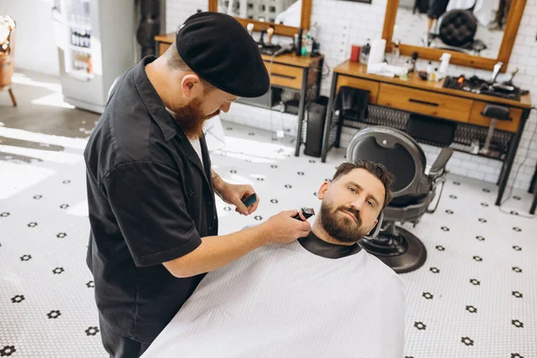 Portrait of professional barber, clipper cutting, shaving beard of regular customer at barbershop. Beauty, selfcare, style, fashion and male cosmetics concept.