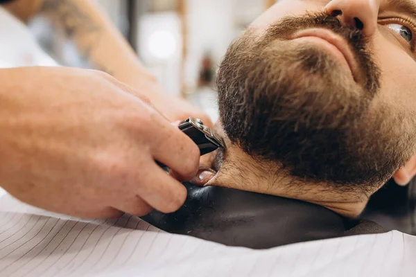 Närbild manliga händer med säkerhet rakhyvel skägg av kund i frisörsalongen. Skönhet, egenvård, stil, mode och manlig kosmetika koncept. — Stockfoto