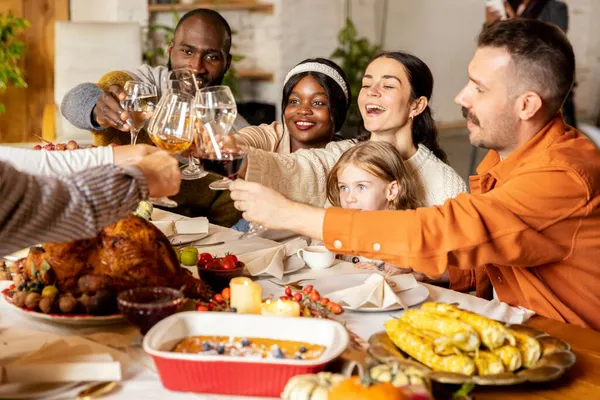 Счастливая семья отмечает День Благодарения, сидя за столом с жареной индейкой и праздничные традиционные блюда, блюда. Питьевое вино — стоковое фото