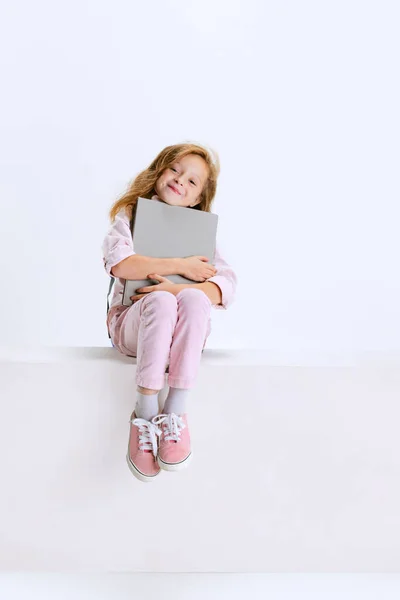 Estudio de tiro de niña linda en ropa casual sentado en la caja grande con enorme libro gris aislado sobre fondo blanco. — Foto de Stock