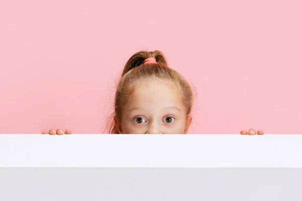 Portret zabawnej uroczej dziewczyny podglądającej zza ściany odizolowanej na różowym tle. — Zdjęcie stockowe