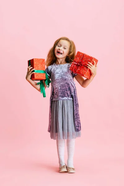 Um feliz bonito caucasiano menina weraing vestido de férias de pé com enorme presente, caixa de presente isolado no fundo do estúdio rosa. — Fotografia de Stock