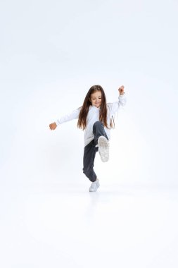 Küçük tatlı bir kızın tam boy portresi, kot pantolonlu kapüşonlu bir çocuk, beyaz stüdyo arka planında izole edilmiş bir şekilde atlıyor..