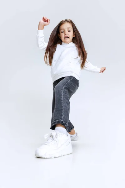 Портрет маленької милої дівчинки, дитина в светрі з джинсами, стрибки ізольовані на білому фоні студії . — стокове фото