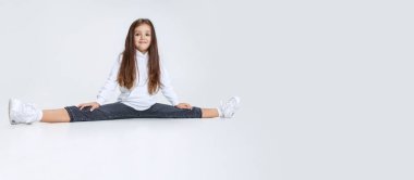 Beyaz atölyenin arka planında izole edilmiş, kot pantolon giymiş ve eğlenen beyaz kız portresi..