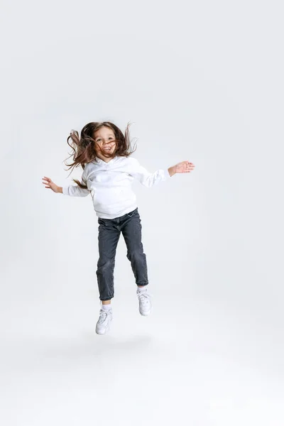 Full-length retrato de menina bonito pouco, criança vestindo capuz com jeans passos, saltos isolados sobre fundo estúdio branco. — Fotografia de Stock
