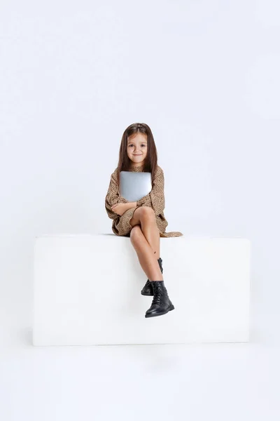 Одна маленькая милая красивая девушка, ребенок в повседневной одежде сидит на большой коробке с цифровой планшет изолированы на белом фоне студии. — стоковое фото
