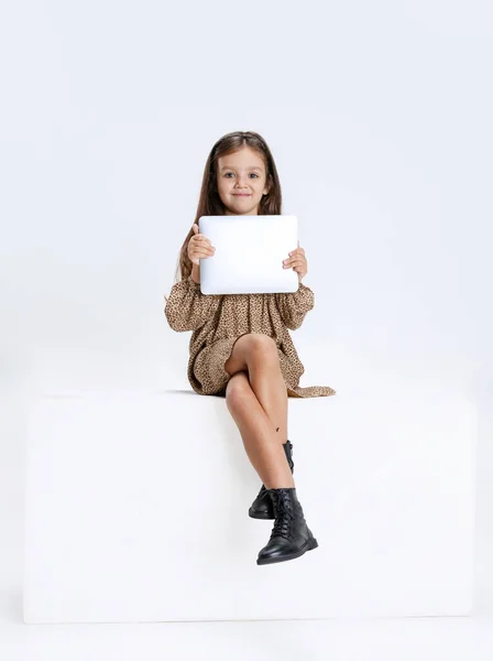 Jedna malá roztomilá krásná dívka, dítě v ležérní šaty sedí na velké krabici s digitálním tabletem izolované na bílém pozadí studia. — Stock fotografie