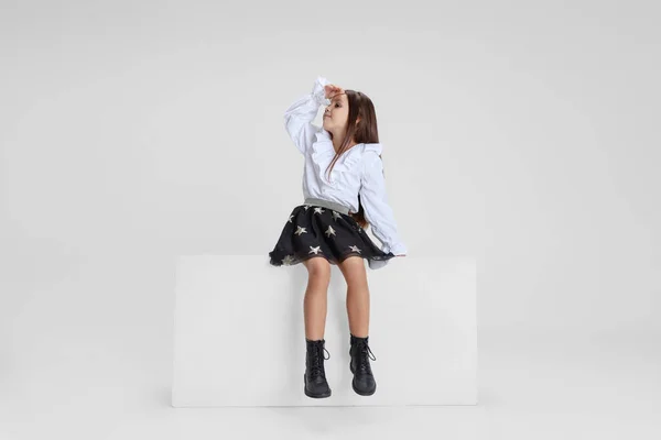 Studio shot van schattig klein meisje in casual kleding zitten op grote doos geïsoleerd op witte achtergrond. — Stockfoto