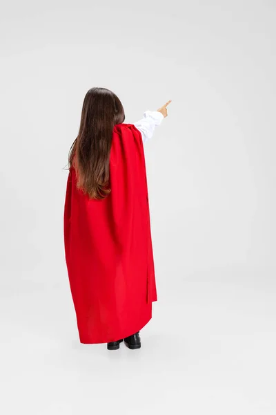 Portret dziewczynki noszącej czerwoną pelerynę stojącej na białym tle studia z przestrzenią do reklam. Widok z tyłu — Zdjęcie stockowe