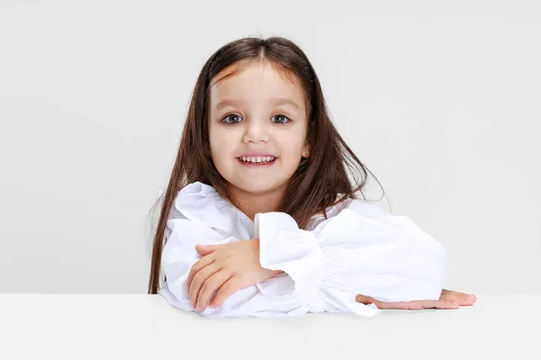 Porträt eines hübschen Schulmädchens, das auf weißem Hintergrund sitzt und in die Kamera schaut. — Stockfoto