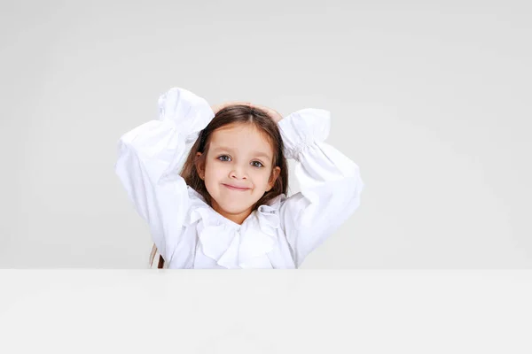 Portret van beuatiful schoolmeisje zitten en kijken naar camera geïsoleerd op witte achtergrond. — Stockfoto