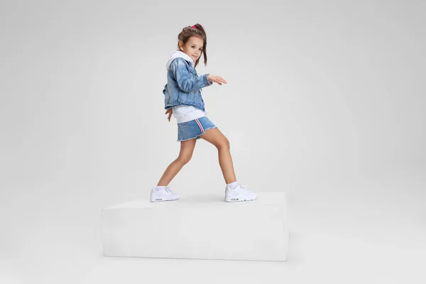 Portrait complet de fille souriante en vêtements décontractés debout sur une grande boîte isolée sur fond de studio blanc. Concept d'enfance heureuse. — Photo