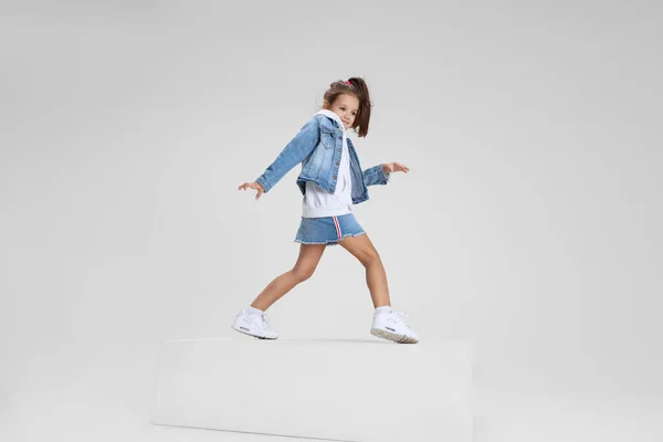 Portrait complet de fille souriante en vêtements décontractés debout sur une grande boîte isolée sur fond de studio blanc. Concept d'enfance heureuse. — Photo