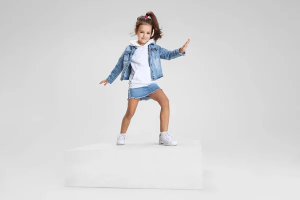 Portrait complet de fille souriante en vêtements décontractés debout sur une grande boîte isolée sur fond de studio blanc. Concept d'enfance heureuse. — Photo