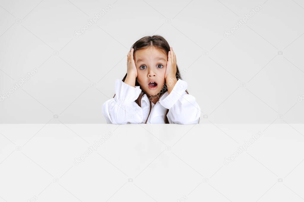 Portrait of beuatiful school girl sitting and looking at camera isolated on white background.