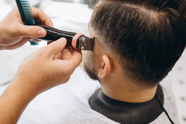 Primer plano peluquero profesional corta el pelo, barba de hombre en la barbería. Belleza, cuidado personal, estilo, moda, salud y cosméticos masculinos concepto. — Foto de Stock