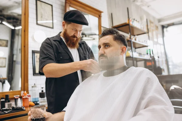 Två stiliga män på frisersalongen. Snygg rödskäggig frisör och klient under klippningsprocessen. Skönhet, sjukvård och manlig kosmetika koncept. — Stockfoto