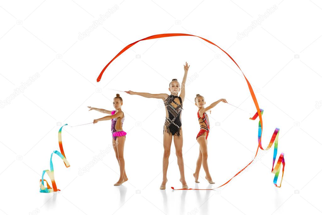 Three-ribbon event. Portrait of little beautiful rhythmic gymnastics artists in group sport event isolated on white studio background.
