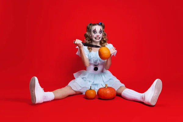 Mulher loira bonita mística em halloween compõem esculpe um sorriso na abóbora isolado sobre fundo vermelho — Fotografia de Stock