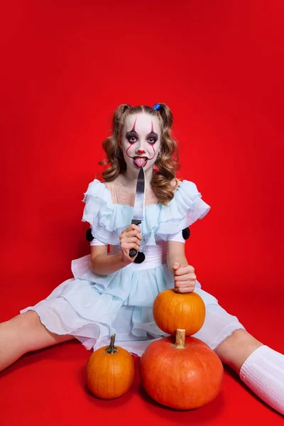 Mystieke blonde vrouw in halloween make-up kijken naar camera met griezelige gezichtsuitdrukking geïsoleerd over rode achtergrond — Stockfoto