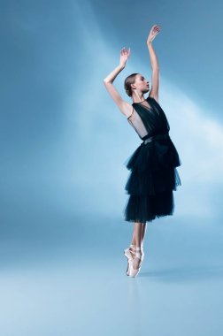 Siyah sahne kıyafetli genç ve zarif balerin, beyaz mavi stüdyo arka planında, neon ışıklarıyla izole edilmiş elbise..