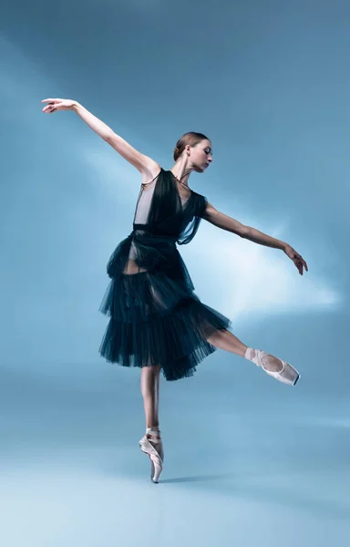 Jonge en sierlijke ballet danser in zwart podium outfit, jurk geïsoleerd op wit blauw studio achtergrond in neon licht. — Stockfoto