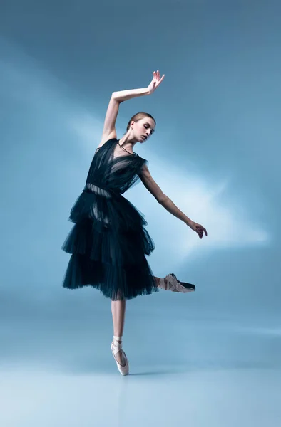 穿着黑色舞服的年轻而优雅的芭蕾舞演员，穿着白色蓝色背景的衣服，在霓虹灯下孤身一人. — 图库照片