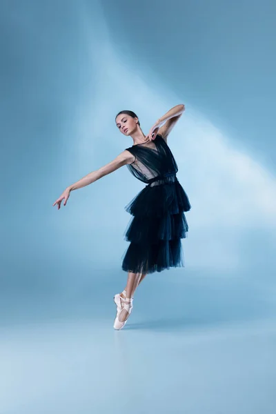 Молодой и грациозный балетный танцор в черном наряде сцены, платье изолировано на белом синем фоне студии в неоновом свете. — стоковое фото