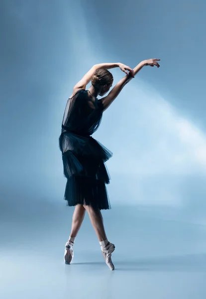 Joven y elegante bailarina de ballet en traje de escenario negro, vestido aislado en fondo blanco estudio azul en luz de neón. — Foto de Stock