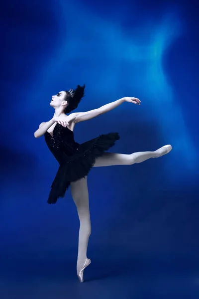 Jedna mladá neuvěřitelně krásná žena, baletka v černém baletu, tutu tančí v modrém studiu plném světla. — Stock fotografie