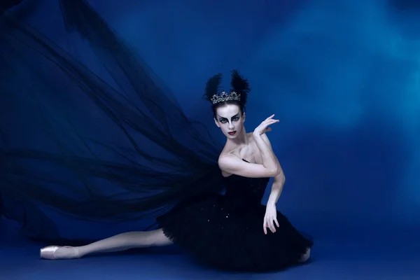 Portret van een schattige vrouwelijke balletdanseres in zwarte tutu en make-up op de vloer geïsoleerd op de rug van een blauwe studio — Stockfoto