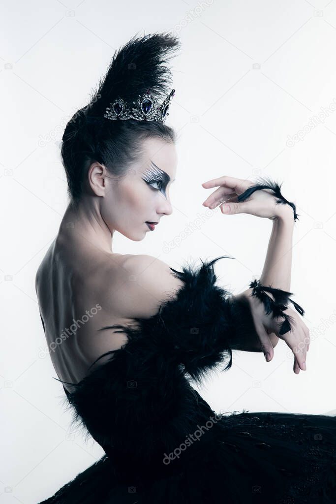 Side view of young ballerina wearing black tutu, stage dress and bright make-up posing isolated on white studio backgorund