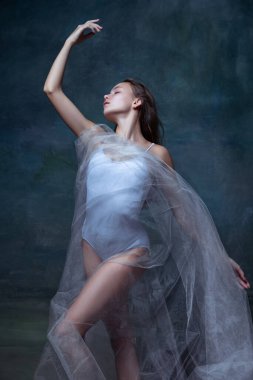 Genç ve güzel bir kızın portresi, beyaz şeffaf kumaşla poz veren bir balerin eskiz stüdyo arka planında izole edilmiş..