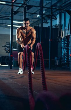 Genç bir adamın ön görüntüsü, kaslı bir sporcu, spor salonunda tek başına vücut geliştirme eğitimi, kapalı alanda. Spor anlayışı, aktivite, sağlıklı yaşam tarzı