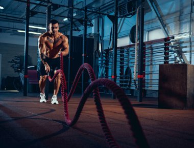 Genç bir adam, kaslı bir atlet spor salonunda vücut geliştirme eğitimi alıyor. Spor anlayışı, aktivite, sağlıklı yaşam tarzı