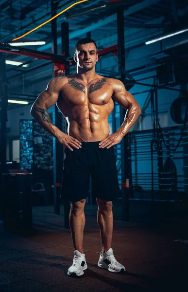 Retrato de homem jovem, atleta musculado, fisiculturista posando no ginásio esportivo, dentro de casa. Conceito de esporte, atividade, estilo de vida saudável — Fotografia de Stock