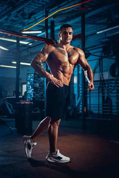 Ritratto di giovane, atleta muscoloso, bodybuilder in posa in palestra, indoor. Concetto di sport, attività, stile di vita sano — Foto Stock