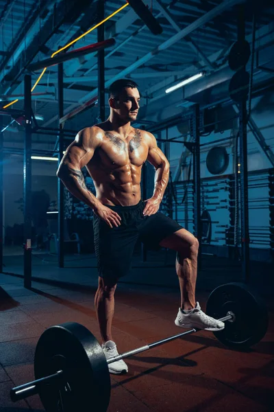 Giovane uomo forte, atleta muscoloso, bodybuilder che si allena da solo in palestra, al chiuso. Concetto di sport, attività, stile di vita sano — Foto Stock